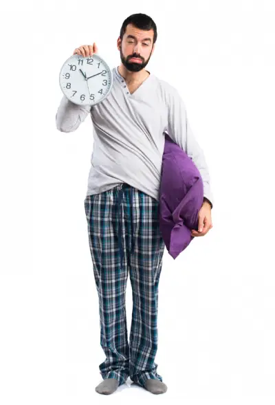 bearded man wearing pajamas holding a clock looking lke he does not get enough sleep